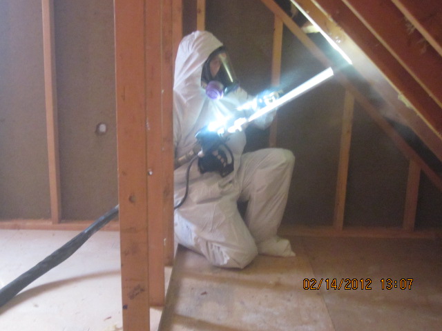 Technician in protective suit spraying attic for mold remediation