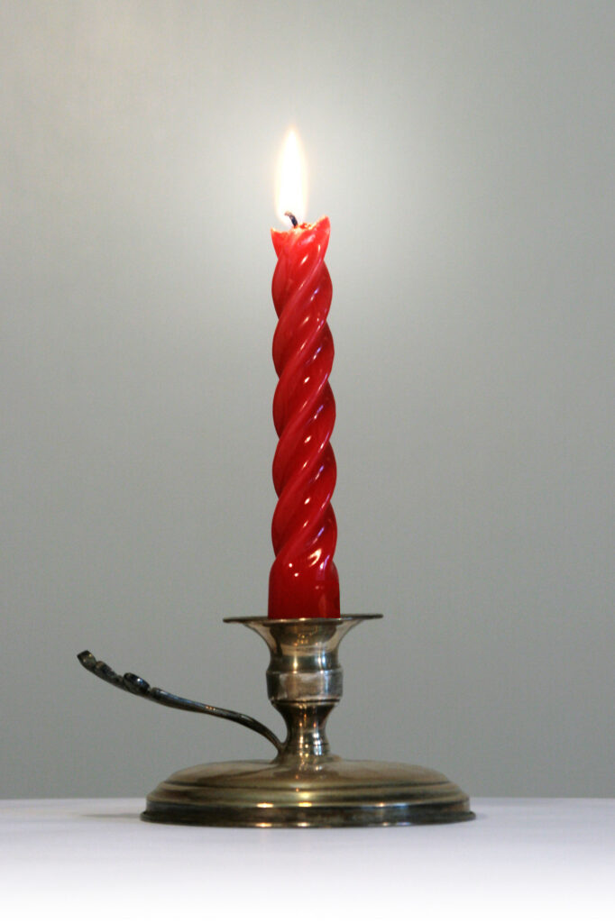 Red taper candle burning in a brass holder