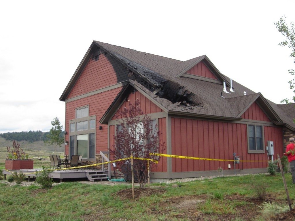Red house with roof fire damage behind caution tape